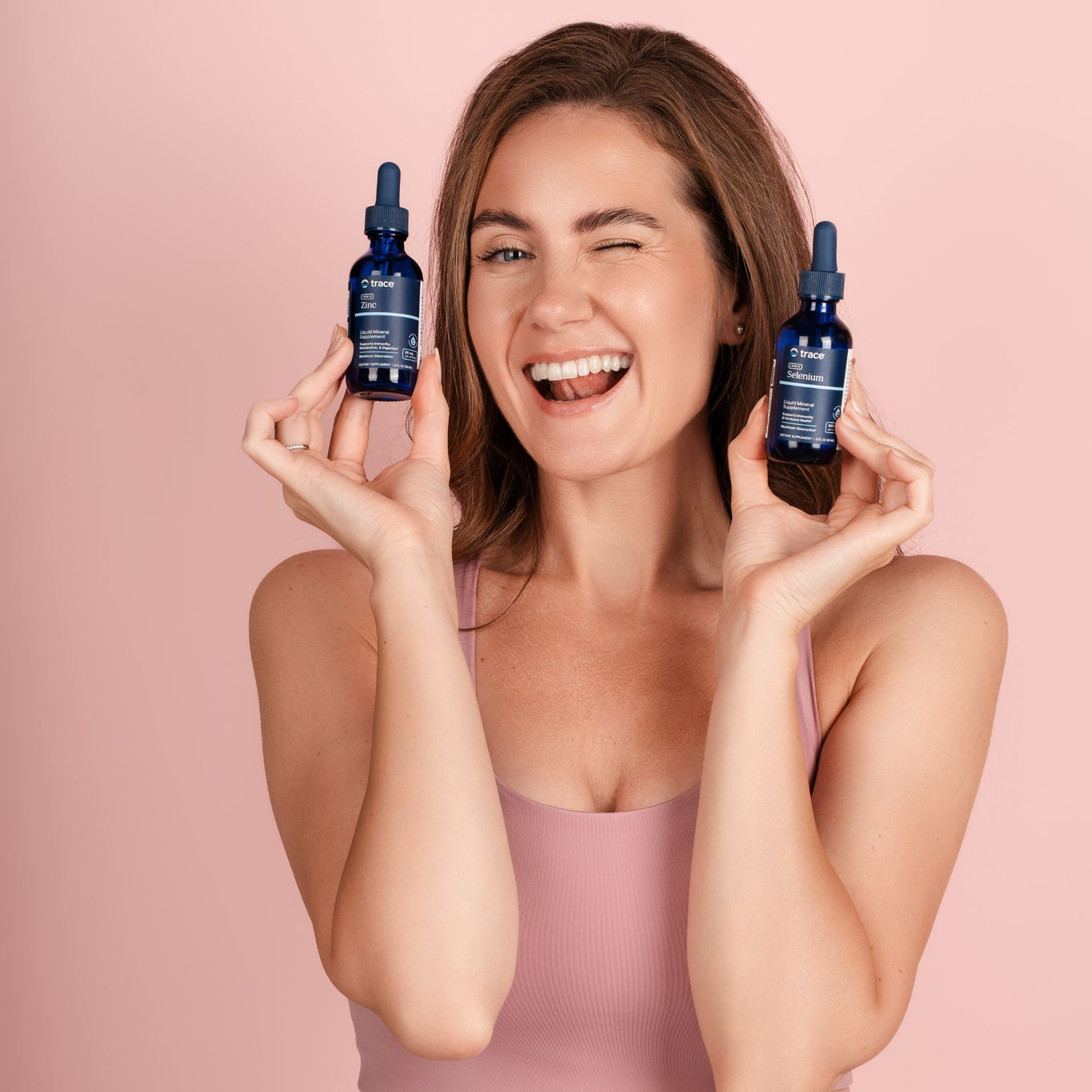 Moteris rausvame fone laiko cinko ir seleno maisto papildų pakuotes.