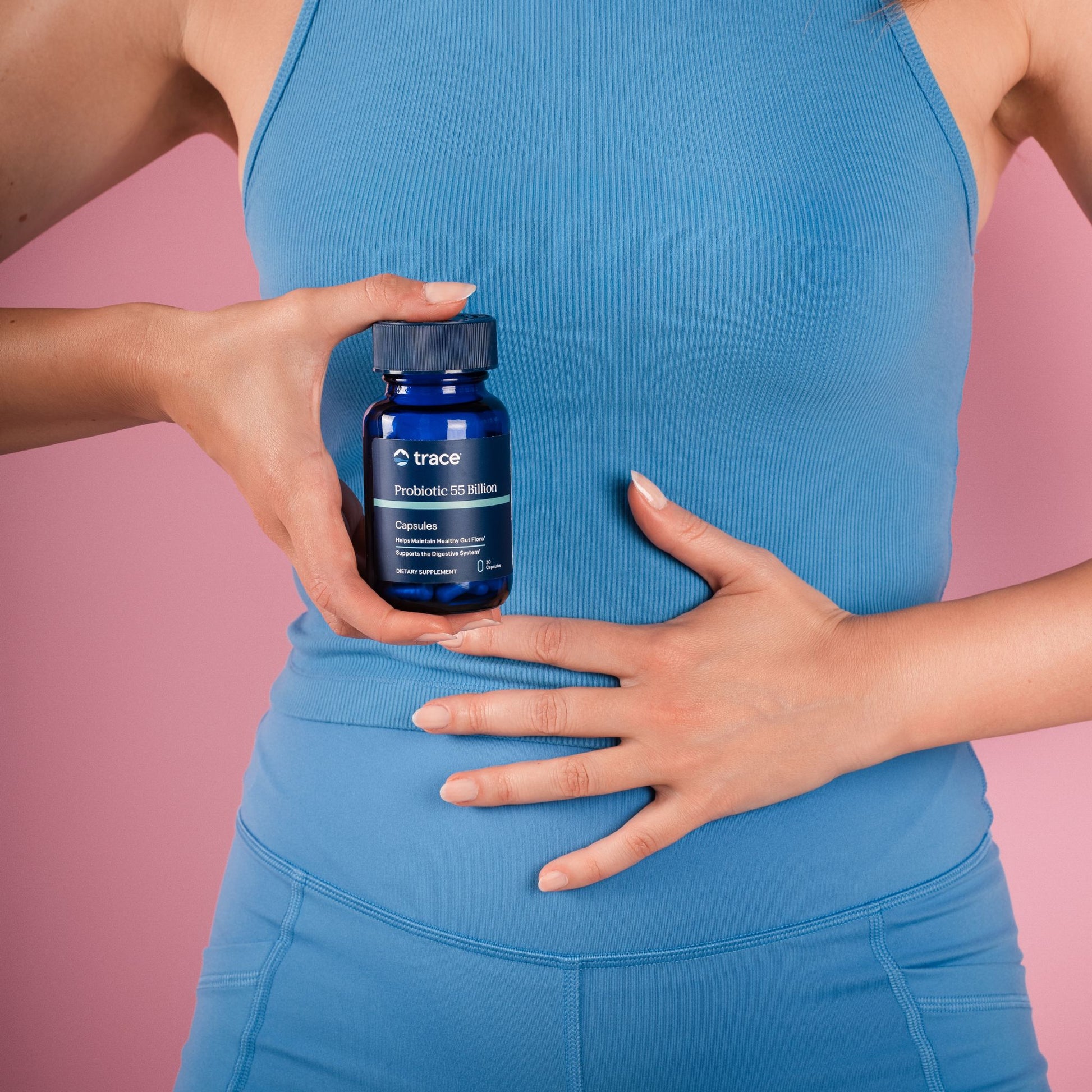 Moteris vienoje rankoje laiko gerųjų bakterijų pakuotę, o kitoje - laikosi už pilvo.